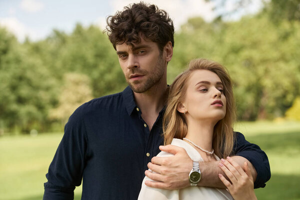 A beautiful young couple in elegant clothing embrace in a lush park, exuding an old money style and rich people lifestyle.