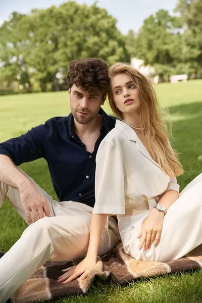 stock image Elegant couple in stylish attire relax on a blanket in a park, showcasing a luxurious outdoor lifestyle.