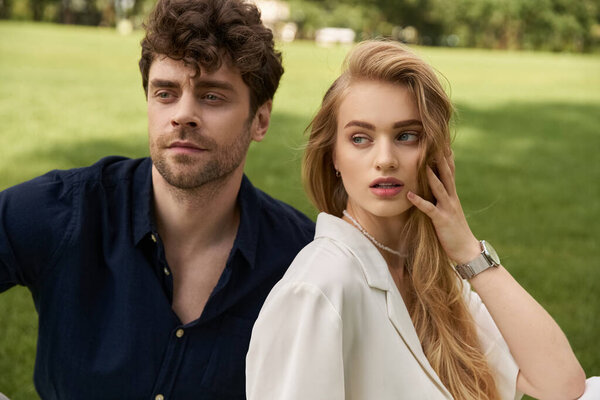 A beautiful young couple in elegant attire sitting on a verdant grassy field, embodying a luxurious and carefree lifestyle.