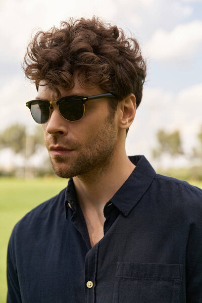 A man with sunglasses stands gracefully in a vast, green field.