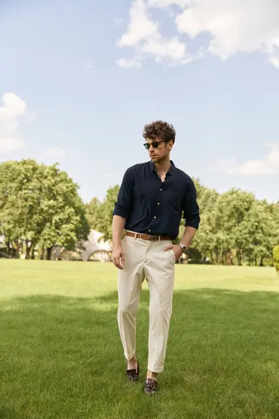 stock image A man in a blue shirt and tan pants leisurely walks through a lush green field, enjoying the peaceful surroundings.