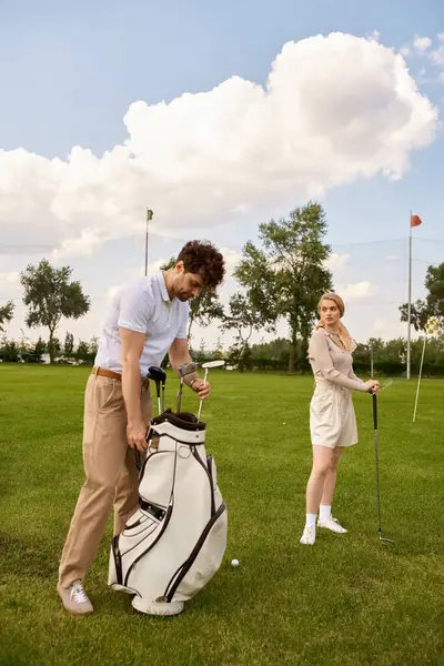 Zarif giyinmiş bir kadın ve erkek, lüks ve sofistike bir şekilde, yemyeşil bir golf sahasında yan yana duruyorlar..