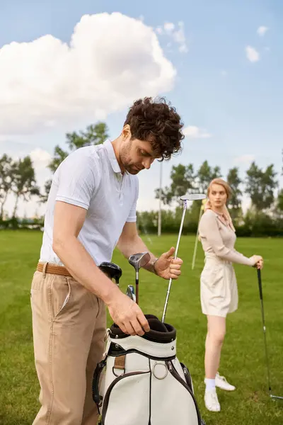 stock image A man and woman in elegant attire stand closely together on a lush green golf course, enjoying a moment of togetherness.