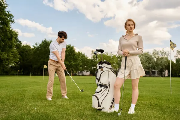 stock image A young couple in elegant attire playing golf on a lush green field at a prestigious club.