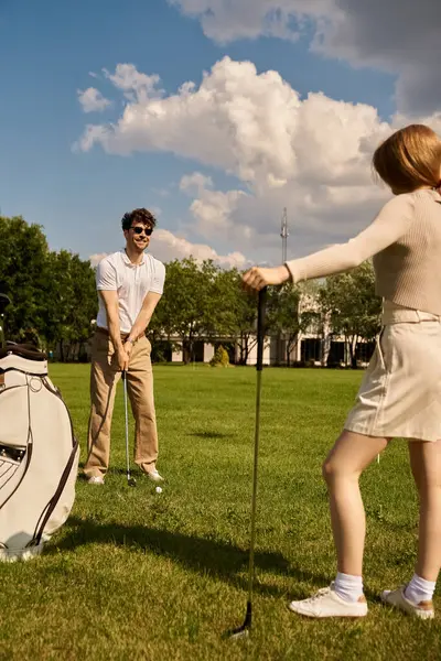 stock image A young couple dressed elegantly playing golf together in a park, enjoying a leisurely day outdoors.