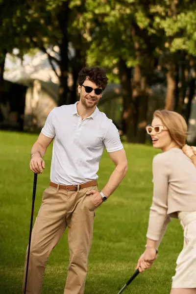 stock image A young couple in elegant attire playing golf in a park, enjoying a leisurely day outdoors together.