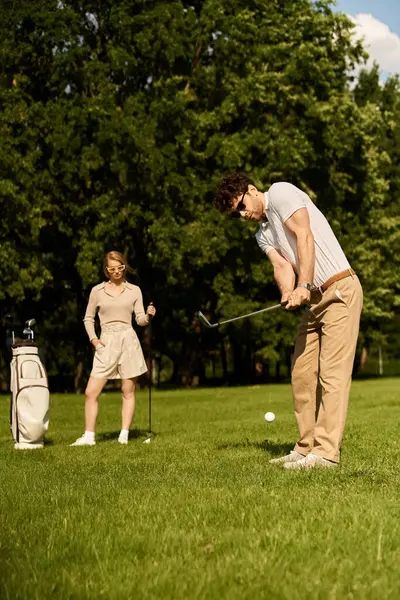 stock image A stylish man and woman in elegant attire enjoying a game of golf in a lush park setting, exuding class and sophistication.