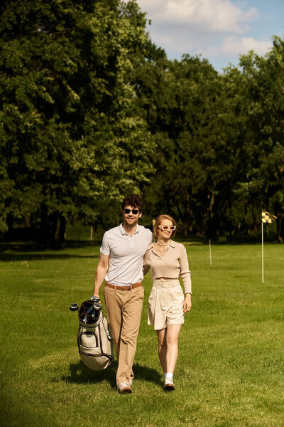 A graceful young couple in elegant attire enjoying a leisurely walk on a picturesque golf course surrounded by lush greenery.