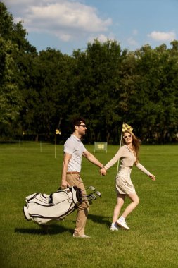 Zarif bir şekilde giyinmiş şık genç bir çift, klasik karmaşıklığın göstergesi olarak yemyeşil bir golf sahasında el ele yürürler..