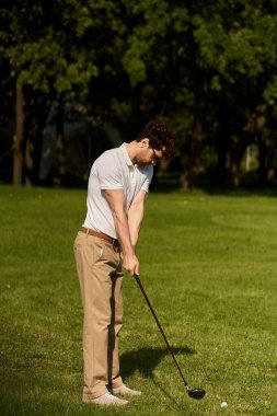 Zarif giyinmiş bir adam golf sopası sallıyor, yemyeşil bir parkta topa vuruyor, lüks bir spor aktivitesinin tadını çıkarıyor..