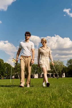 Zarif giyinmiş genç bir adam ve kadın yemyeşil bir golf sahasında birlikte yürüyorlar, lüks bir açık hava aktivitesinin tadını çıkarıyorlar..