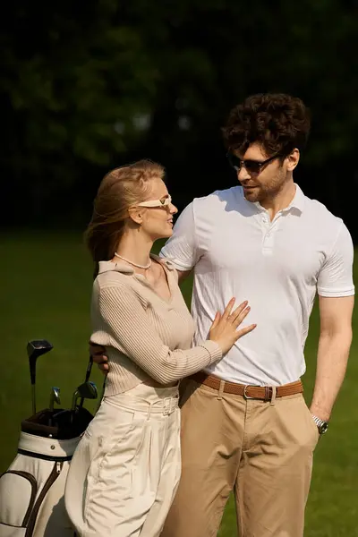 stock image A stylish man and woman in elegant attire pose on a lush golf course, exuding sophistication and leisure.