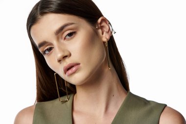 Uzun siyah saçlı güzel bir kadın yeşil bir üst ve altın küpeler içinde gri bir fona karşı zarif bir poz verir..