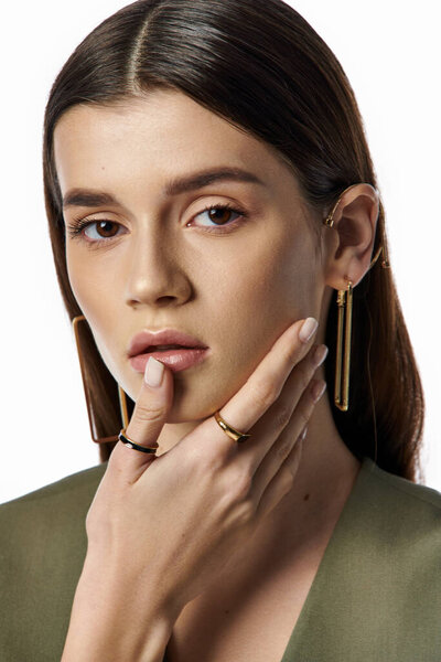 A beautiful woman with long dark hair in stylish attire, thoughtful expression, and hand on her chin poses on a gray backdrop.