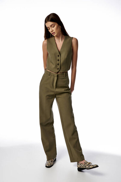 A fashionable woman with long dark hair poses in a stylish green jumpsuit and leopard print shoes on a gray backdrop.