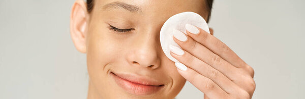 A stylish, vibrant teenage girl holds cotton pad to her face with curiosity and wonder.