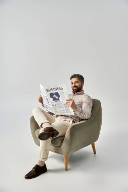 An elegant man with a beard sits in a chair, engrossed in reading a newspaper. clipart