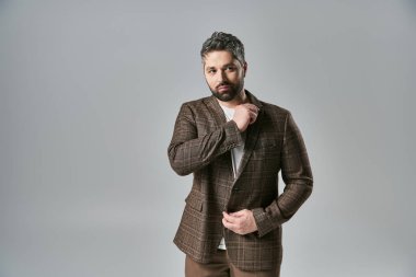 Sakallı çekici bir adam, gri bir stüdyo geçmişine karşı şık bir poz verir..