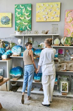 Two women, a loving lesbian couple, stand together in an art studio. clipart