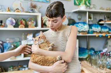 Bir kadın nazikçe bir kediyi kollarına alır..