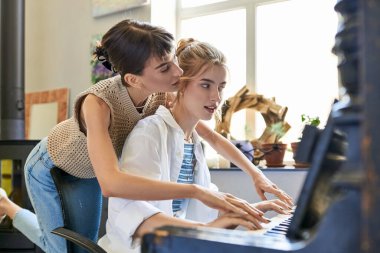 Tender moments shared as two young women play piano together in an art studio. clipart