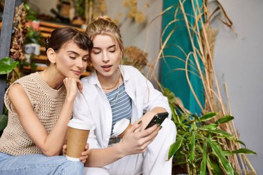 Tender lesbian couple share a moment, engrossed in cell phone. clipart