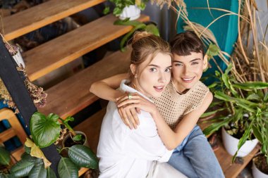 A peaceful moment as two women sit on a bench in front of lush green plants. clipart