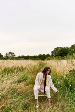 A young woman in white attire sitting on a chair in a serene field, basking in the warm summer breeze. clipart