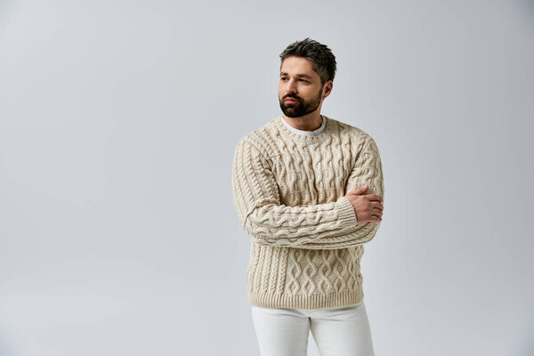 A stylish man with a beard striking a pose in a white sweater against a grey studio backdrop.