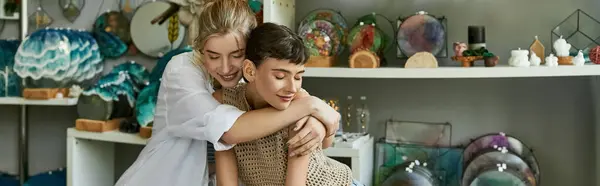 stock image Two women embrace in an art studio surrounded by delicate glassware.
