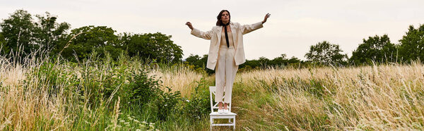 A young woman in white attire stands on a chair, embracing the summer breeze in a peaceful field.
