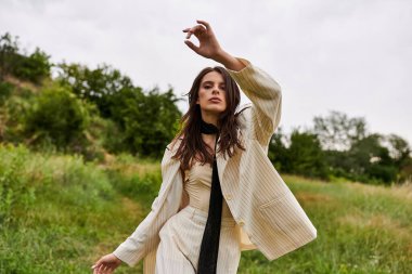 Beyaz elbiseli güzel bir kadın bir tarlada zarif bir şekilde duruyor yaz rüzgarının hafifçe okşadığını hissediyor..