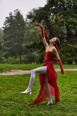 A young woman in a stunning red dress gracefully dances in the rain, feeling the summer breeze. clipart