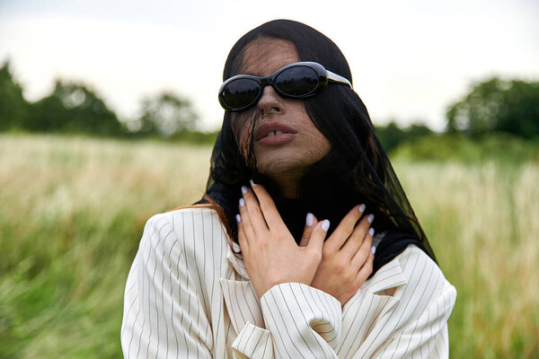 A beautiful young woman in a veil and sunglasses enjoys the summer breeze in a field of nature.