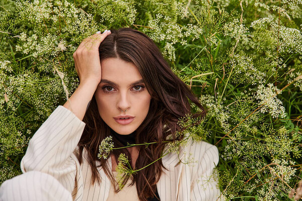 A young woman in white attire sits in the grass with hands on head, enjoying the summer breeze in a vast field.