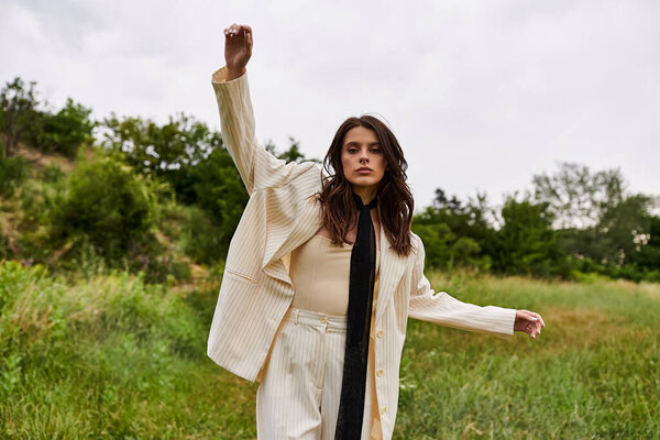 A beautiful young woman in white attire stands in a field with her arms raised, basking in the warmth of the summer sun.