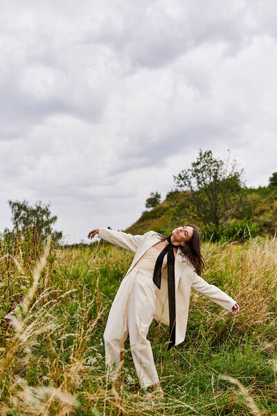 A young woman stands in a field, arms outstretched, wearing white attire, feeling the summer breeze and embracing the beauty of nature.