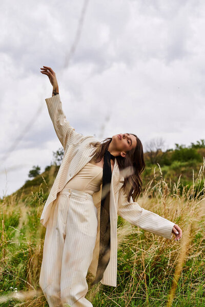 A beautiful young woman in white attire standing in a field of tall grass, feeling the summer breeze on her face.