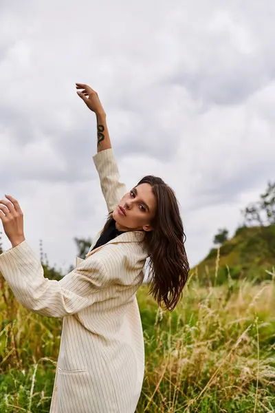 stock image A beautiful young woman in white attire stands in a field, enjoying the summer breeze.