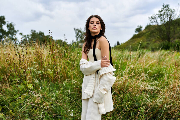 A beautiful young woman in white attire standing gracefully in a field of tall grass, basking in the summer breeze.