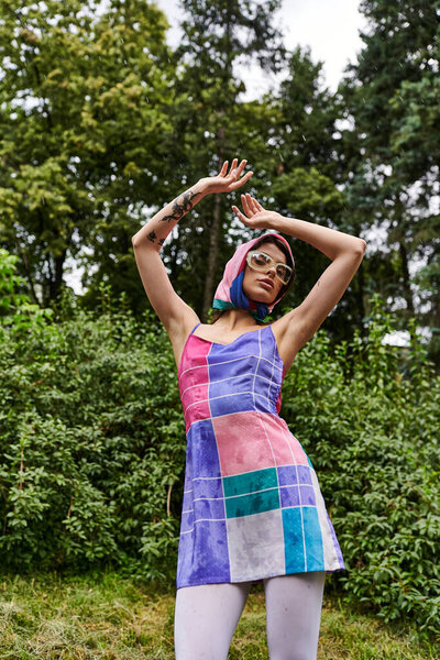 A beautiful young woman in a colorful dress and sunglasses, standing gracefully in the lush green grass, enjoying the summer breeze.