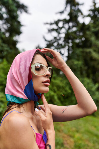 A beautiful young woman in a vibrant pink and blue scarf and stylish sunglasses, enjoying the summer breeze in nature.