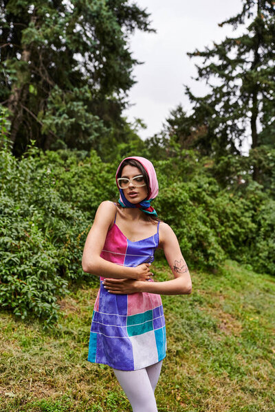 A young woman in a colorful dress and sunglasses dancing gracefully in a vibrant field, enjoying the summer breeze.