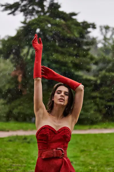 stock image A beautiful young woman in a red dress and long gloves revels in the summer breeze in nature.