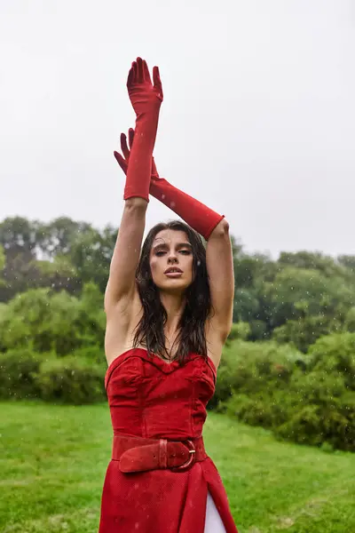 stock image A young woman in a striking red dress and long gloves savors the summer breeze in a natural setting.