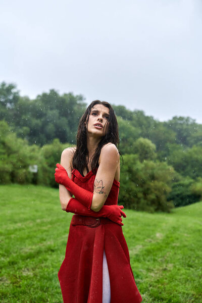 A stunning woman in a crimson dress and gloves, soaking in the summer breeze amidst a vast field.