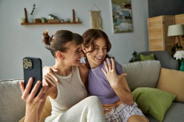 İki kadın, güzel bir lezbiyen çift, kanepede oturmuş neşeyle selfie çekiyorlar..
