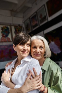 Two mature women hugging in an art studio. clipart