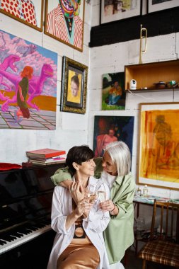 İki kadın, olgun lezbiyenler, bir sanat stüdyosunda kuyruklu piyanonun başında duruyorlar..