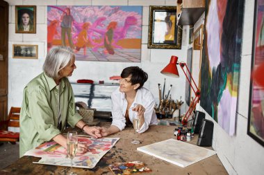 Two woman discussing artwork at table in studio. clipart